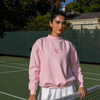 Woman in a Baby Pink CourtLife Tennis Mock Neck with pink crossed racquet embroidery and a white skirt at a tennis net
