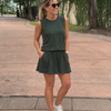 Woman in sunglasses wearing a green CourtLife Pique Tank with a matching skort, walking outdoors on a paved driveway