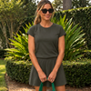 Woman in sunglasses wearing a green CourtLife Pique Tee and matching green skort in a garden, holding a tote handle