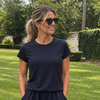 Smiling woman in sunglasses wearing a navy CourtLife Pique Tee with cap sleeves and a navy skort on a grassy lawn